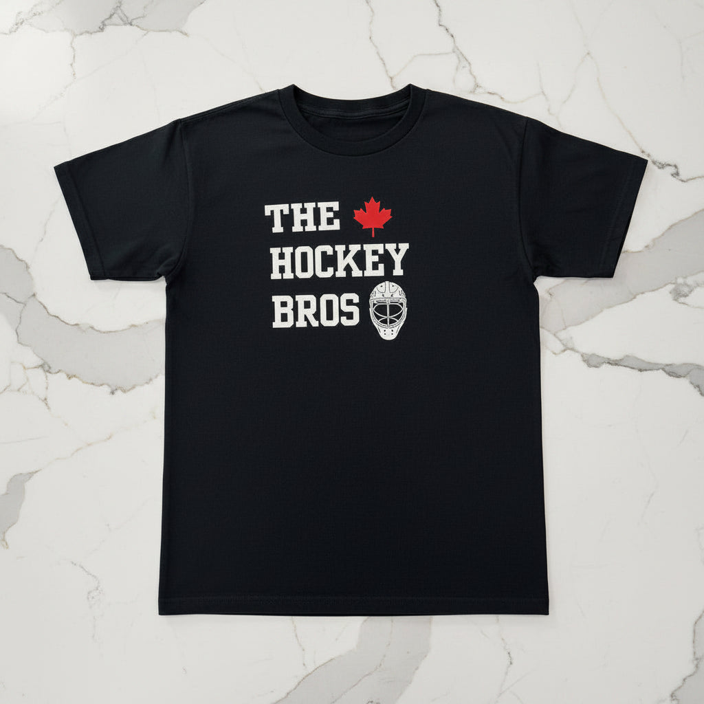 A black short-sleeve t-shirt with a graphic on the chest that reads 'THE HOCKEY BROS' in white block letters, accompanied by a small red maple leaf and a white hockey goalie mask illustration, displayed flat against a light gray background.